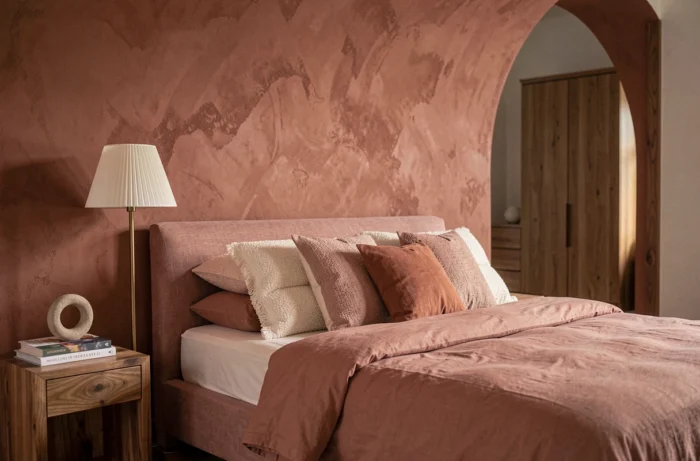 Chambre principale apaisante avec tête de lit en lin rose, mur arrondi en enduit terracotta et accessoires en laiton selon les tendances déco 2024